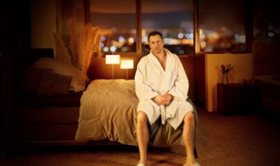 Andy Ost im Bademantel auf Bett sitzend, führt zum Kalendereintrag