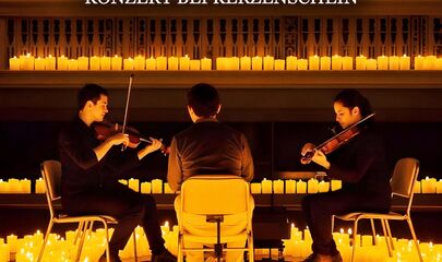 Drei Musiker zwischen vielen Kerzen auf einer Bühne, führt zum Kalendereintrag